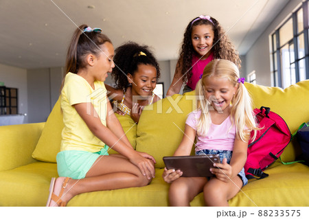 Cheerful multiracial elementary schoolgirls using digital table while sitting on couch Cheerful multiracial elementary schoolgirls using digital table while sitting on couch 88233575