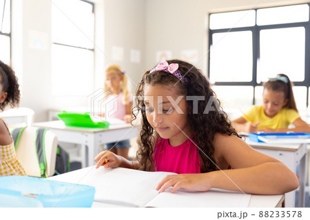 Multiracial elementary schoolgirls studying at desk in classroom Multiracial elementary schoolgirls studying at desk in classroom 88233578