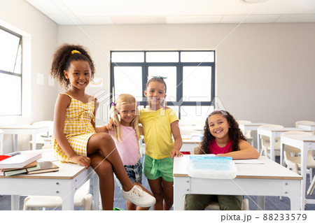 Portrait of smiling multiracial elementary schoolgirls at desk in classroom 88233579