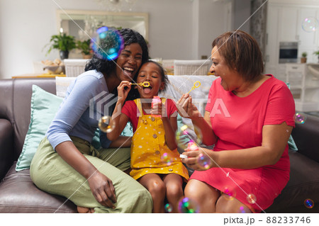 Playful african american girl blowing bubbles with mother and grandmother at home 88233746