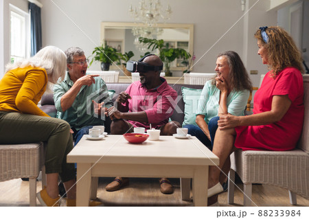 Happy multiracial senior man and women looking at male friend using vr headset at home Happy multiracial senior man and women looking at male friend using vr headset at home 88233984