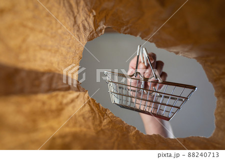 A hand places a shopping cart in a paper bag. A mature man's hand holds an empty shopping cart over an open brown bag. Shot from the bottom up. Close up. Selective focus A hand places a shopping cart in a paper bag. A mature man's hand holds an empty shopping cart over an open brown bag. Shot from the bottom up. Close up. Selective focus 88240713