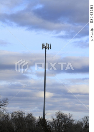 A 5 G  cell phone tower with trees and a colorful blue sky with clouds. 88243165