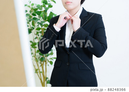 朝に姿見鏡で服装をチェックするスーツの若い女性　身だしなみ　着替える　パンツスーツ 88248366