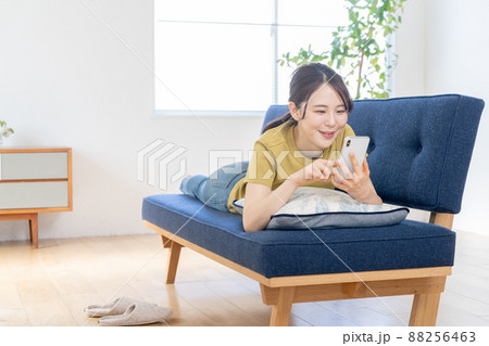 リビングのソファに寝っ転がってスマホを操作する若い女性 リビングのソファに寝っ転がってスマホを操作する若い女性 88256463