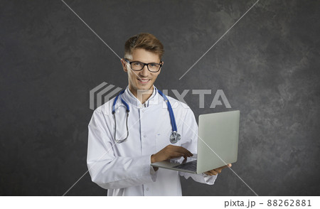 Portrait of happy male healthcare worker standing with laptop in hands on gray background. Portrait of happy male healthcare worker standing with laptop in hands on gray background. 88262881
