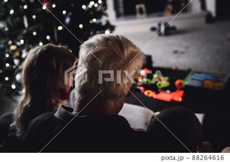 Grandpa reading a storybook to two grandkids sitting on his lap Grandpa reading a storybook to two grandkids sitting on his lap 88264616