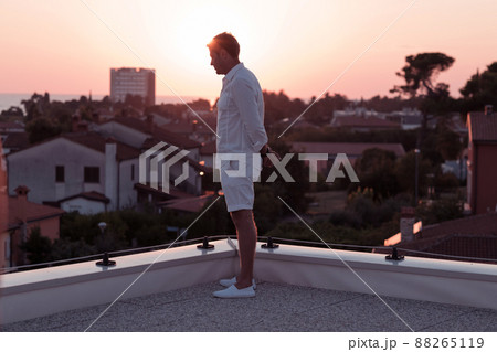 an elderly businessman in casual clothes enjoys the roof of his house at sunset time. Selective focus  88265119