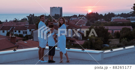 Happy family enjoys and spends time together on the roof of the house while watching the sunset on the open sea together Happy family enjoys and spends time together on the roof of the house while watching the sunset on the open sea together 88265177