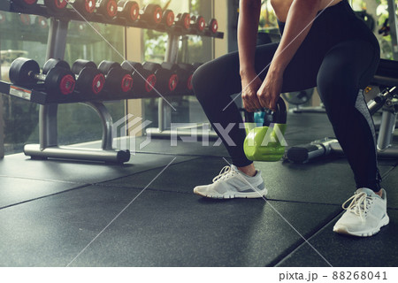 Woman exercising with kettlebell while being in squats position at the gym. Woman exercising with kettlebell while being in squats position at the gym. 88268041