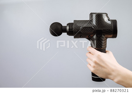 Close-up of a female hand with a portable massager gun on a white background. Close-up of a female hand with a portable massager gun on a white background. 88270321