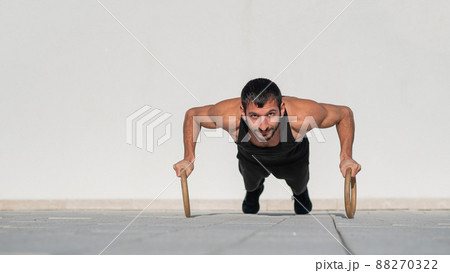 A man in black sportswear doing ring push-ups outdoors. A man in black sportswear doing ring push-ups outdoors. 88270322