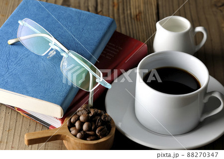珈琲豆が入ったスプーンと珈琲が入ったコーヒーカップとソーサ―と眼鏡と本 珈琲豆が入ったスプーンと珈琲が入ったコーヒーカップとソーサ―と眼鏡と本 88270347