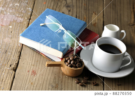 珈琲豆が入ったスプーンと珈琲が入ったコーヒーカップとソーサ―と眼鏡と本 珈琲豆が入ったスプーンと珈琲が入ったコーヒーカップとソーサ―と眼鏡と本 88270350