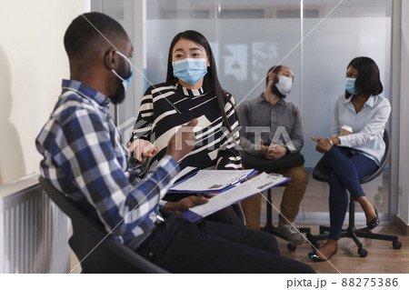 Multi ethnic people with CV resumes sitting in lobby area of financial company while waiting to be chosen for interview. Man and woman in waiting room talking about agency internal regulations. Multi ethnic people with CV resumes sitting in lobby area of financial company while waiting to be chosen for interview. Man and woman in waiting room talking about agency internal regulations. 88275386