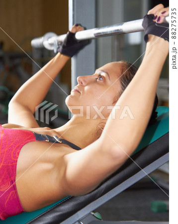 Getting a toned and fit body. Shot of an attractive young woman lifting a barbell in the gym. Getting a toned and fit body. Shot of an attractive young woman lifting a barbell in the gym. 88275735