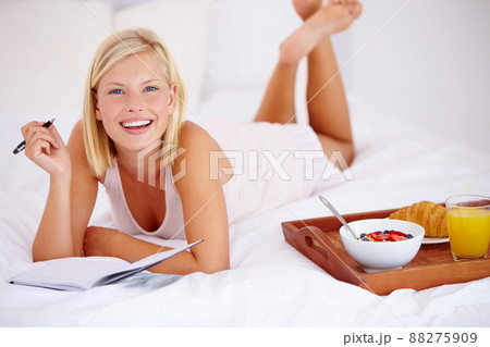 She has her day all planned out. Blonde woman lying on her bed and writing in her diary with her breakfast next to her. 88275909