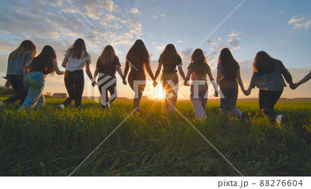 A group of girls walk towards the sun at sunset holding hands. 88276604
