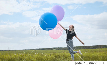 Happy girl with big multicolored balloons posing on the field. Happy girl with big multicolored balloons posing on the field. 88276694