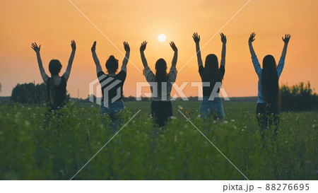 Girls friends waving their hands to the setting sun at sunset. Girls friends waving their hands to the setting sun at sunset. 88276695