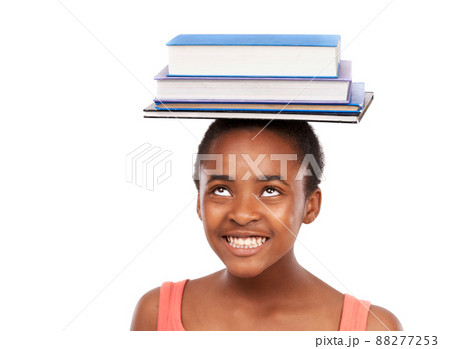 Perfecting my balance. Studio shot of a young african girl balancing books on her head isolated on white. 88277253