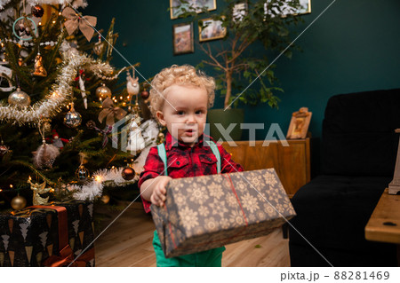 A two-year-old little boy carries a gift package on Christmas Day. A two-year-old little boy carries a gift package on Christmas Day. 88281469