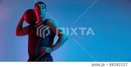 Portrait of young Korean man with basketball ball looking away isolated on blue studio background in neon light. Youth, hobby, sport concepts. 88282227