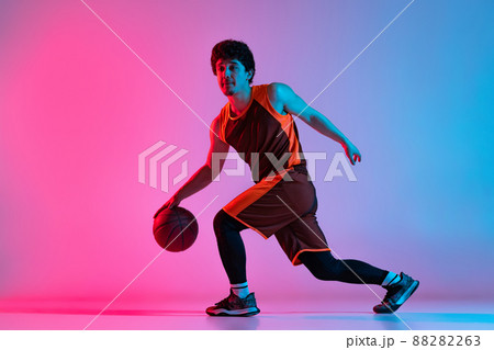 Sportive man playing basketball isolated on gradient pink blue studio background in neon light. Youth, hobby, motion, activity, sport concepts. 88282263