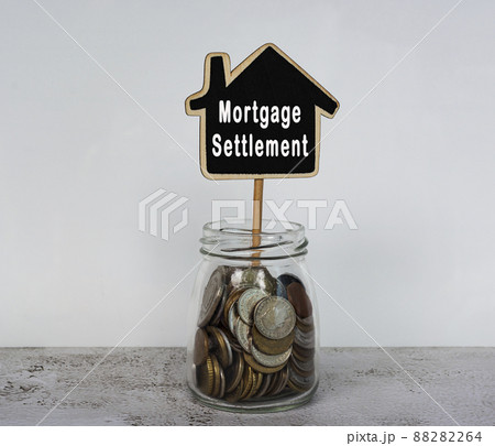 Mortgage settlement text on wooden house model with jar full of coins on a desk 88282264