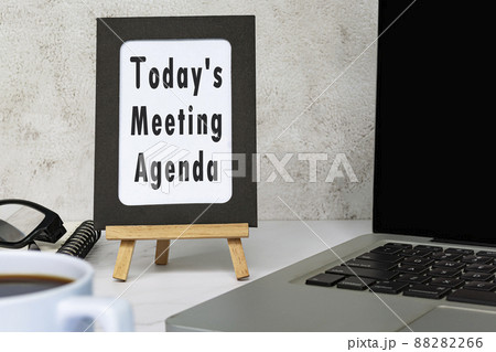Today's meeting agenda text written on chalkboard with notebook on white desk. 88282266