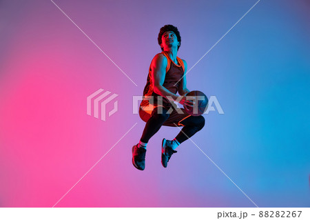Young energetic man playing basketball isolated on gradient pink blue studio background in neon light. Youth, hobby, motion, activity, sport concepts. 88282267