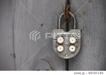 Old combination padlock hanging on grungy gray wooden door 88285180
