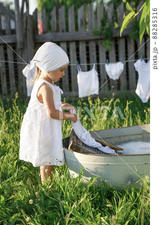 Baby washes clothes in the village in the garden in a basin on an old washing board. Bleach and detergents for white linen. Rustic retro style. 88285316