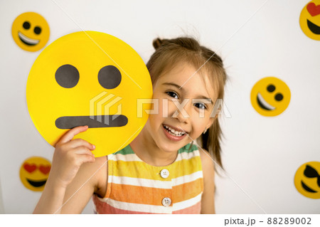 A happy, cheerful girl looks out from behind a unhappy cardboard smile face. Be positive no matter what. A sanguine person. Temperament A happy, cheerful girl looks out from behind a unhappy cardboard smile face. Be positive no matter what. A sanguine person. Temperament 88289002