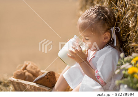 a healthy childhood in harmony with nature. happy little baby in folk clothes sits on a wheat field with a jar of fresh milk. the sun's rays are reflected in a jar of fresh, tasty milk a healthy childhood in harmony with nature. happy little baby in folk clothes sits on a wheat field with a jar of fresh milk. the sun's rays are reflected in a jar of fresh, tasty milk 88289994