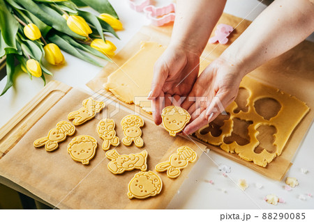 Woman cutting pastry dough into Easter egg shape while making sugar cookies. Holidays baking. Top view 88290085