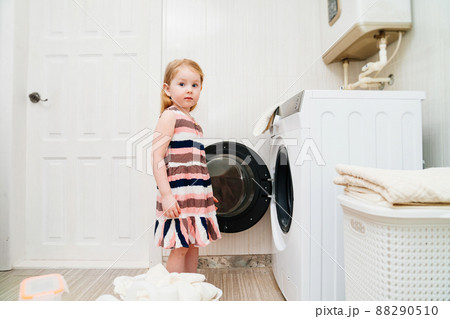 a cute little girl with laundry near the washing machine.  88290510