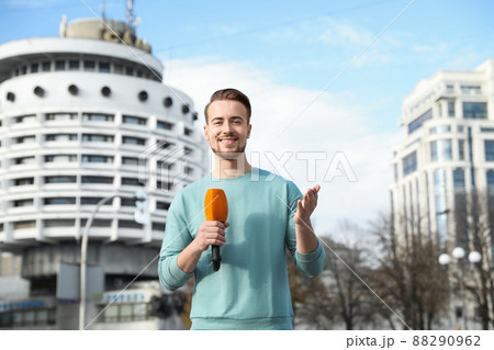 Young male journalist with microphone working on city street Young male journalist with microphone working on city street 88290962
