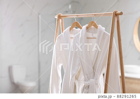 Fresh white bathrobes hanging on rack indoors 88291265