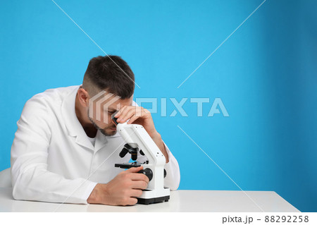 Scientist using modern microscope at table against blue background, space for text. Medical research Scientist using modern microscope at table against blue background, space for text. Medical research 88292258