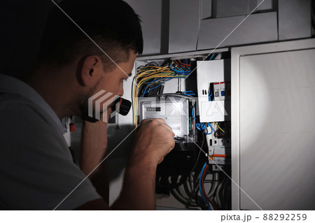 Electrician with flashlight fixing electric panel indoors Electrician with flashlight fixing electric panel indoors 88292259