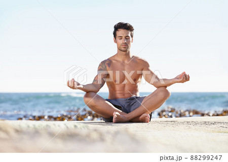 Seeking enlightenment in nature. A young man meditating next to the ocean. Seeking enlightenment in nature. A young man meditating next to the ocean. 88299247