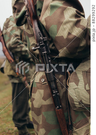 A man in a soldier's co-ornate uniform with a rifle carbine on his shoulder during a reconstruction of military action 88299292
