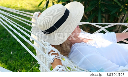 female in a straw hat is resting in a hammock around the palm trees and enjoying the tranquility and female in a straw hat is resting in a hammock around the palm trees and enjoying the tranquility and 88301593