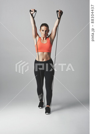 Raising her game. Studio portrait of an athletic young woman working out with a resistance band against a grey background. 88304437