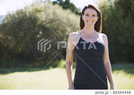 The outdoors is a place of rest for her. An attractive woman in sports clothing smiling while standing in the outdoors. The outdoors is a place of rest for her. An attractive woman in sports clothing smiling while standing in the outdoors. 88304448