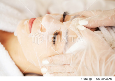 Cosmetologist applying sheet mask on woman in spa salon 88305826