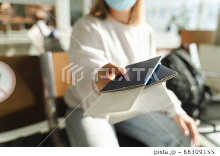 Woman in a mask sits in the waiting room and holds out her passport and ticket to the camera	 88309155
