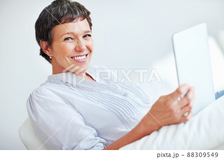 Smiling woman using digital tablet at home. Portrait of smiling mature woman using tablet PC while sitting on couch. Smiling woman using digital tablet at home. Portrait of smiling mature woman using tablet PC while sitting on couch. 88309549