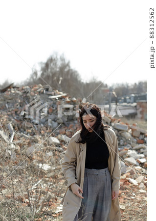 A lonely girl in a coat and jeans on the ruins of a ruined house. consequences of the war grain effect 88312562